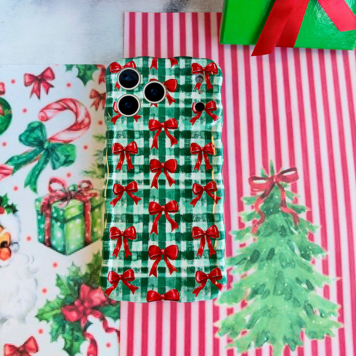 Plaid Tidings & Bows iPhone case lying flat on red and white striped paper beside a watercolor Christmas tree