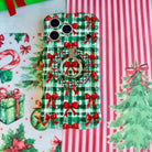 Close-up of the Plaid Tidings & Bows MagSafe grip ring on the matching gingham bow iPhone case, on red and white striped paper