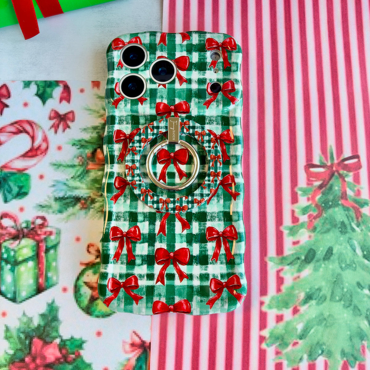 Close-up of the Plaid Tidings & Bows MagSafe grip ring on the matching gingham bow iPhone case, on red and white striped paper