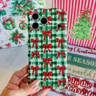 Hand holding the Plaid Tidings & Bows Wavy Luxe MagSafe iPhone case, red bows on green and white gingham, beside Merry Christmas and Joy to the World signs