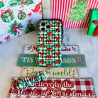 Plaid Tidings & Bows iPhone case and gingham bow scrunchie wrist strap on stacked wooden Christmas signs with a green gift box