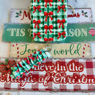 Plaid Tidings & Bows scrunchie phone wrist strap clipped below the matching gingham bow iPhone case on wooden Christmas signs