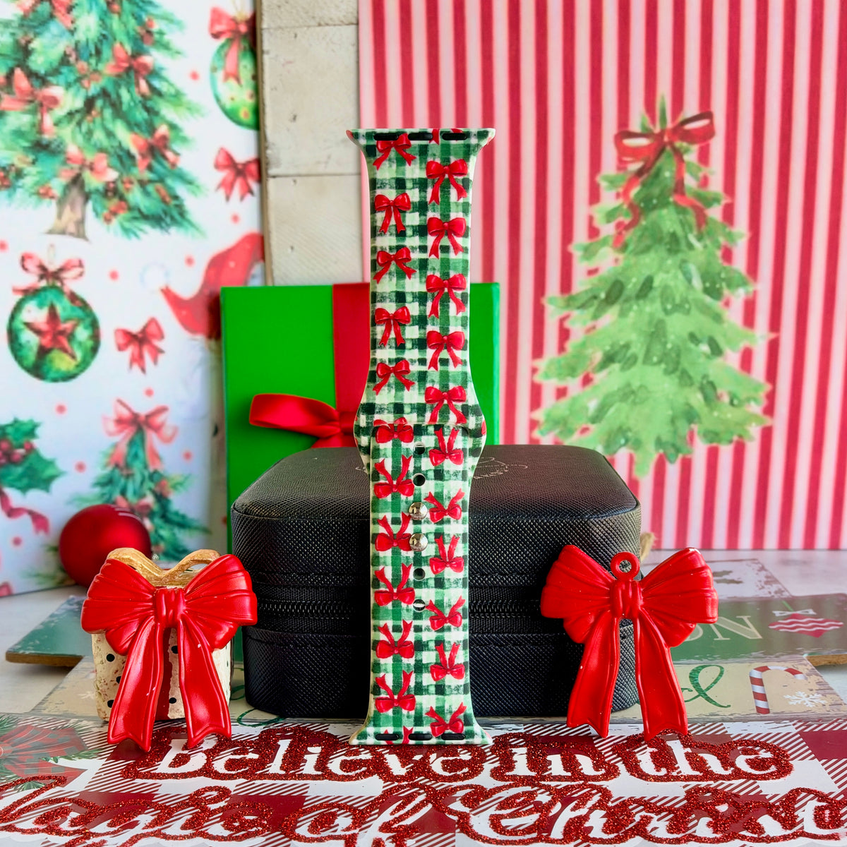 Plaid Tidings & Bows Apple Watch band buckled and standing on a black jewelry box between red bow ornaments