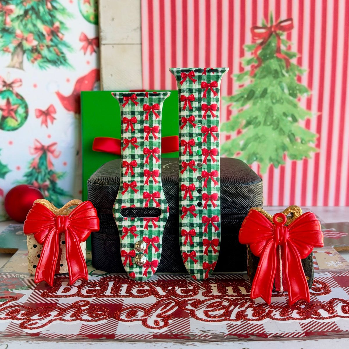 Both straps of the Plaid Tidings & Bows silicone Apple Watch band on a black jewelry box between two red bow ornaments