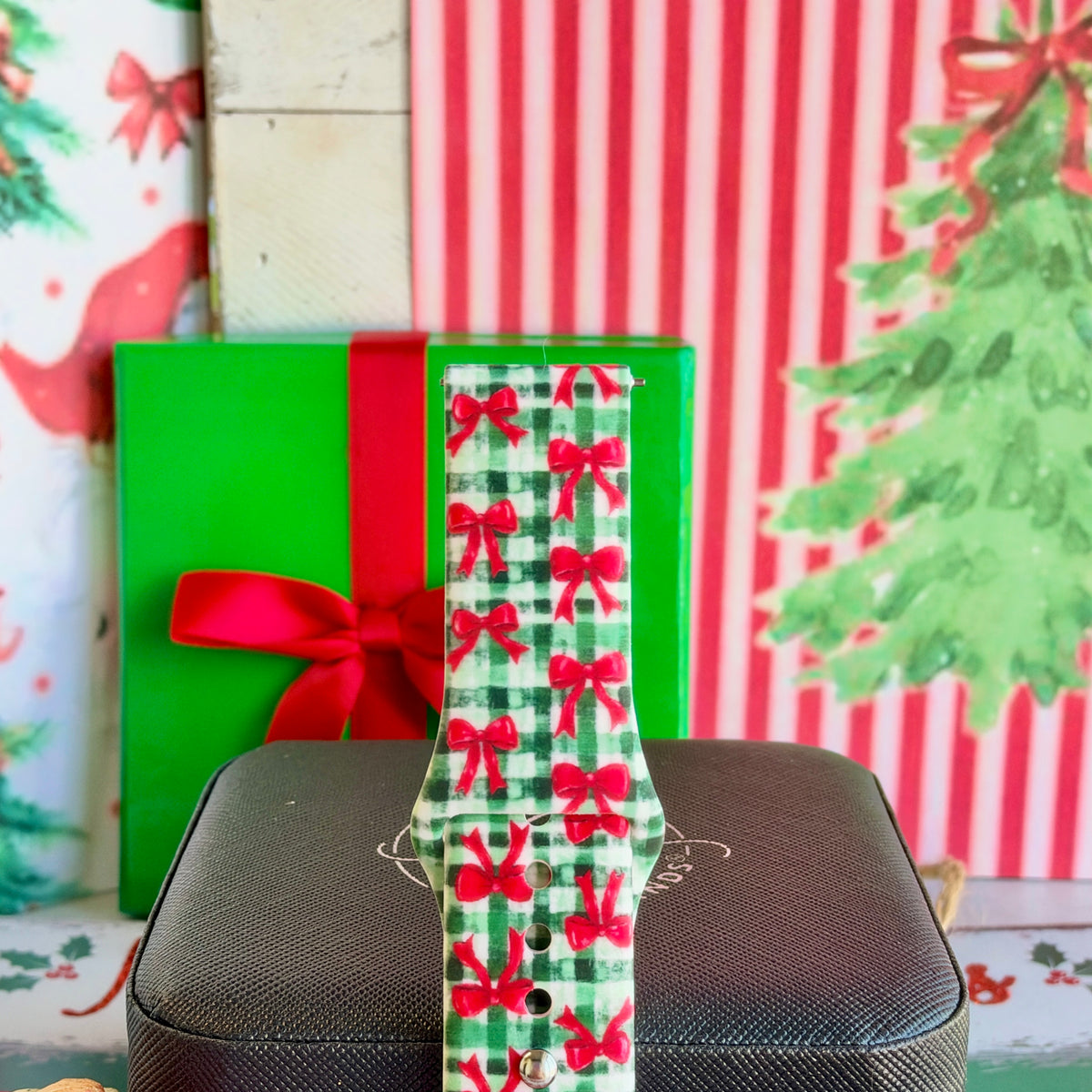 Single Plaid Tidings & Bows Samsung watch band strap standing on a black jewelry box in front of a green gift box