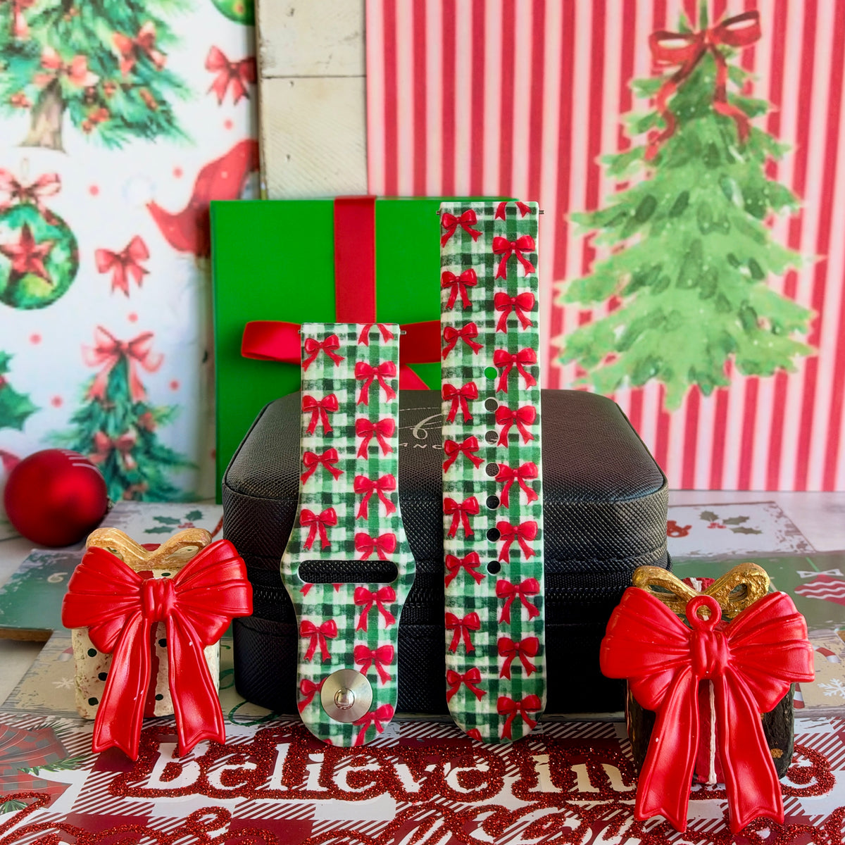 Both straps of the Plaid Tidings & Bows silicone Samsung Galaxy Watch band on a black jewelry box between red bow ornaments
