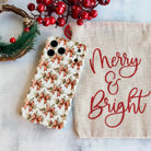 Deck Yourself in Bows & Holly iPhone case lying flat beside a Merry & Bright linen bag, a pine wreath and red berries