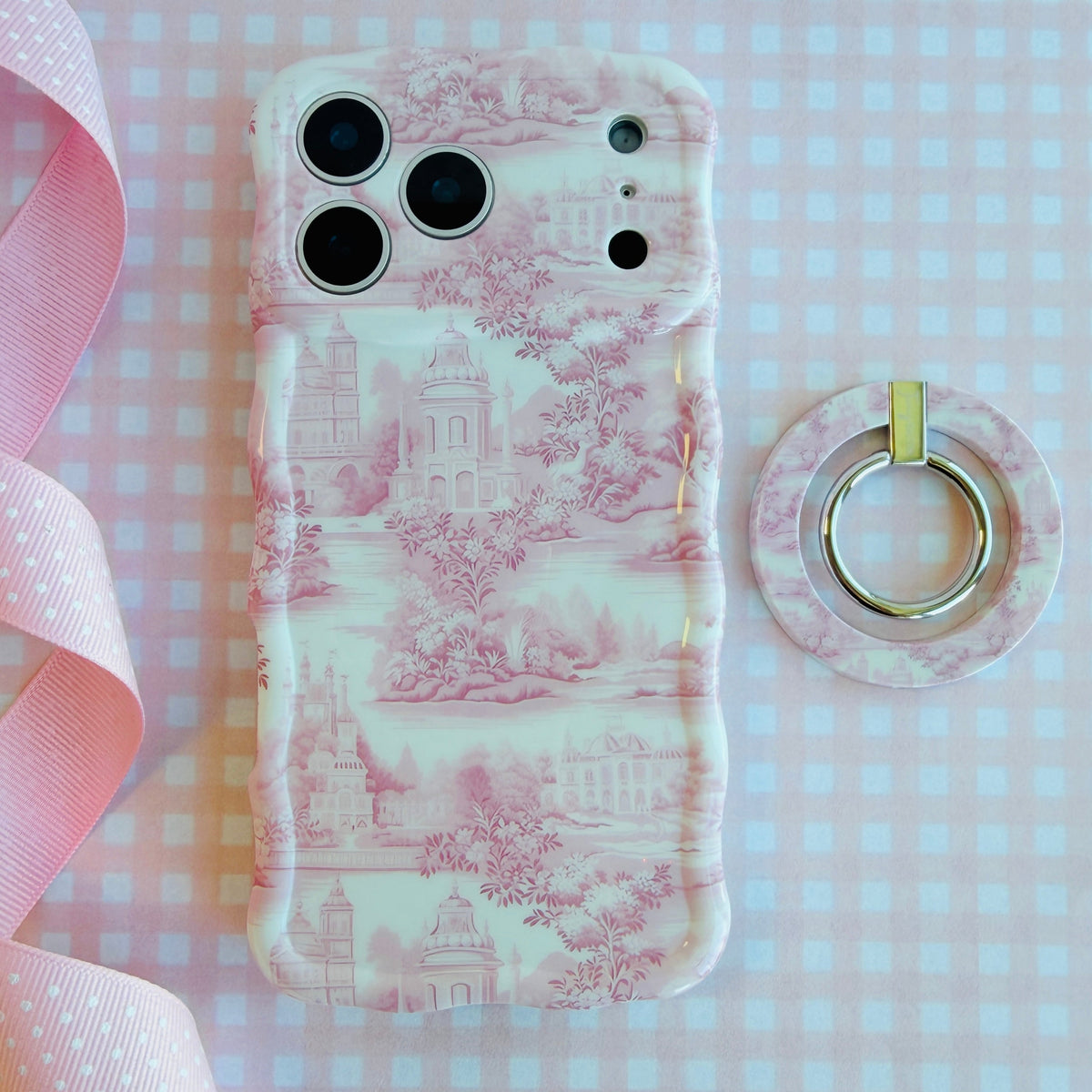Blush Manor Hold It Fancy MagSafe grip ring resting beside the matching pink toile Wavy Luxe iPhone case, with a pink ribbon on a pastel gingham backdrop