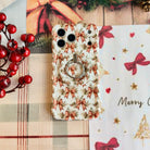 Close-up of the Deck Yourself in Bows & Holly MagSafe grip ring on the matching bow-print iPhone case, on cream plaid with red berries