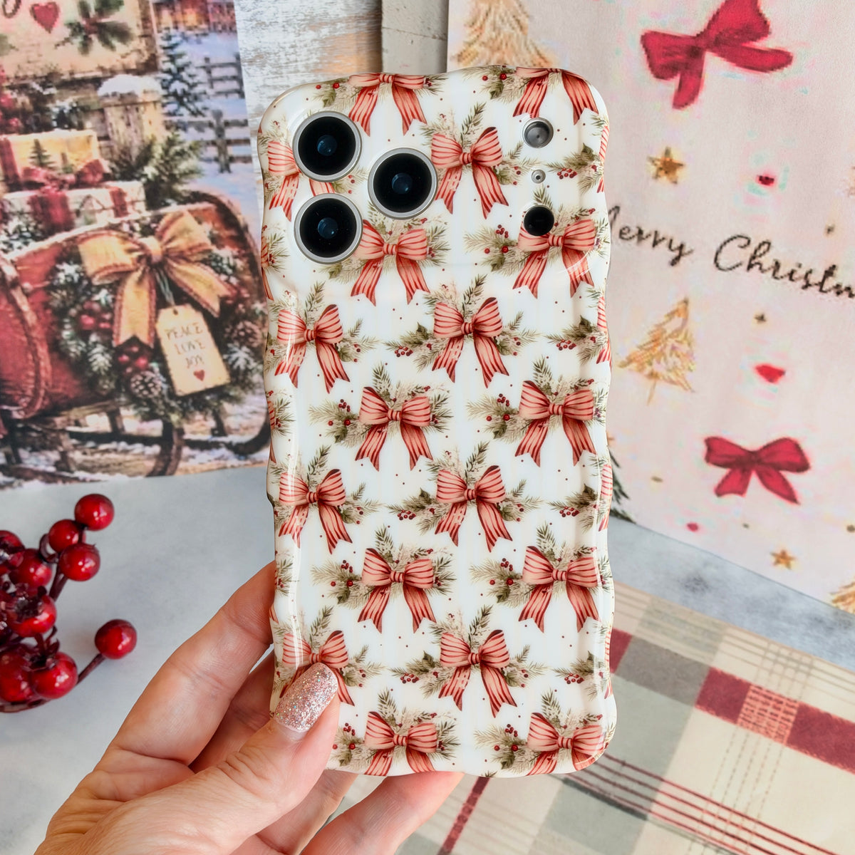 Hand holding the Deck Yourself in Bows & Holly Wavy Luxe MagSafe iPhone case, striped red ribbon bows with pine and holly on ivory, beside vintage sleigh art and plaid