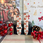 Both straps of the Deck Yourself in Bows & Holly silicone Apple Watch band on a black jewelry box with red berries and a pinecone