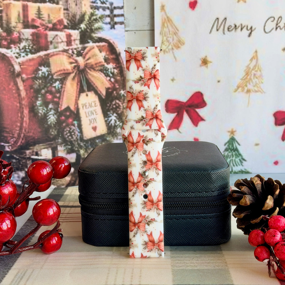 Deck Yourself in Bows & Holly Samsung Galaxy Watch band buckled and standing on a black jewelry box between red berries and a pinecone