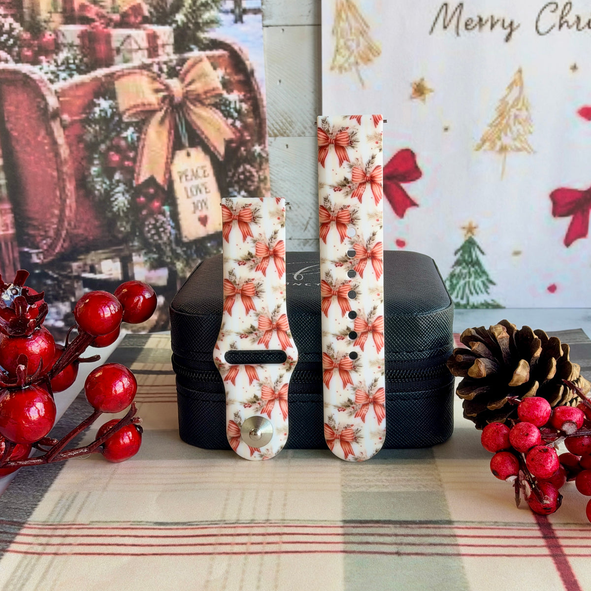 Both straps of the Deck Yourself in Bows & Holly silicone Samsung Galaxy Watch band on a black jewelry box with red berries and a pinecone