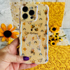 Hand holding the Bee Happy Wavy Luxe MagSafe iPhone case with honeybees and rainbows on a honey-cream background