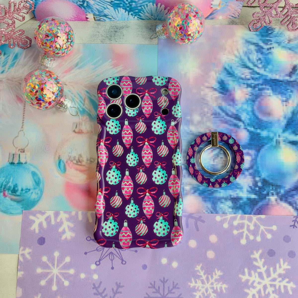 Just One More Ornament MagSafe grip ring lying beside the matching iPhone case on lavender snowflake paper with confetti ornaments