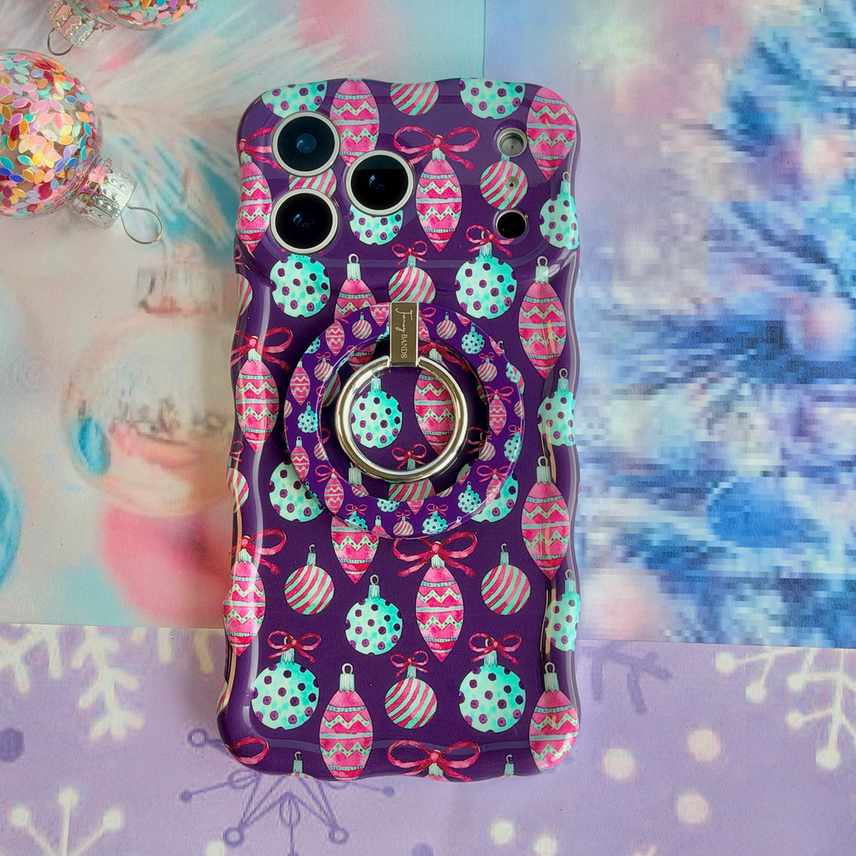 Just One More Ornament MagSafe grip ring snapped onto the matching purple ornament iPhone case, on aqua tinsel with pink glitter snowflakes