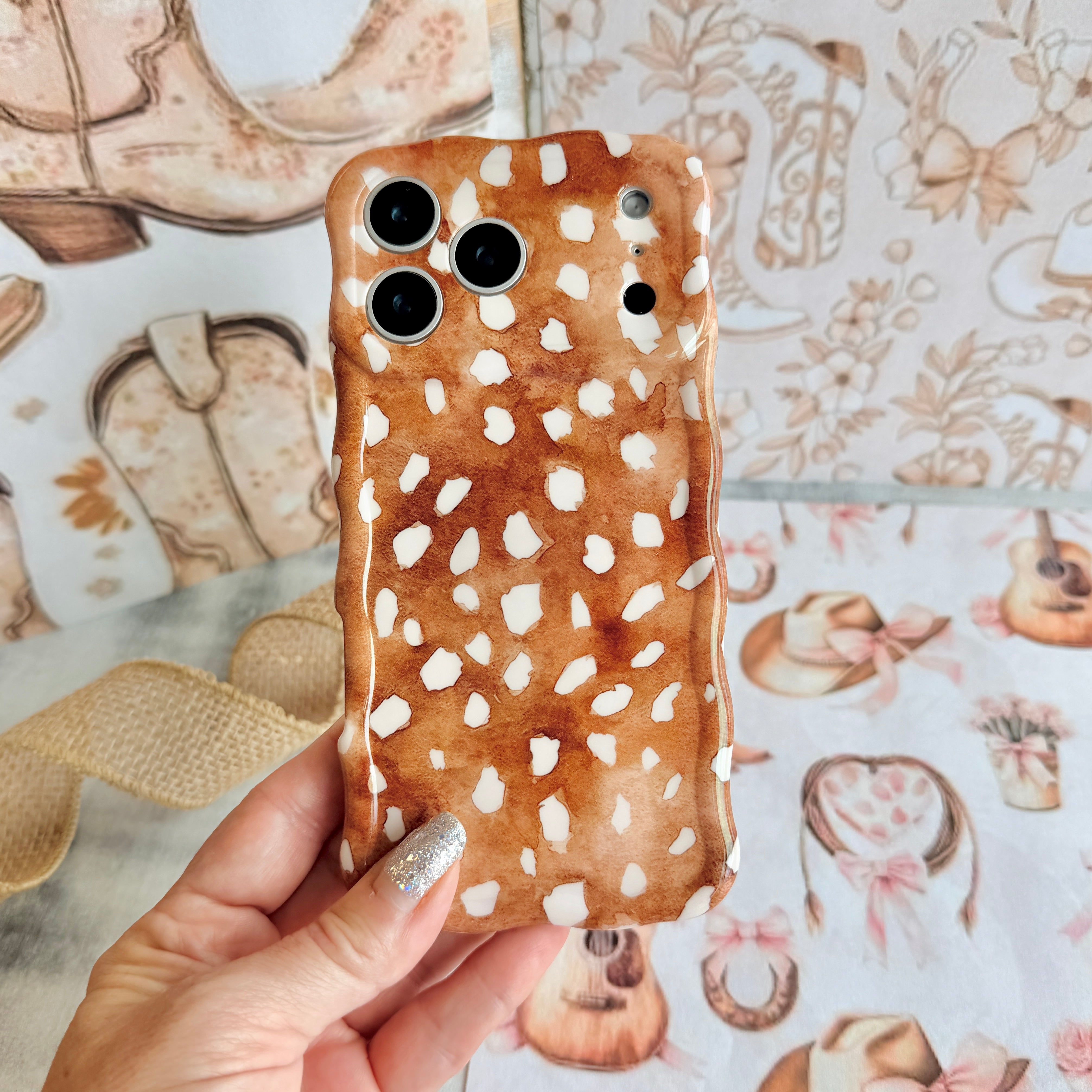 Warm whiskey-brown wavy iPhone case featuring a white fawn-spotted pattern with a high-gloss finish.