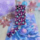 Just One More Ornament iPhone case with its ornament-print scrunchie wrist strap on lavender snowflake paper and aqua tinsel, beside a pink glitter snowflake