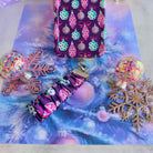 Just One More Ornament scrunchie phone wrist strap clipped below the matching iPhone case on aqua tinsel, with pink glitter snowflakes and confetti ornaments