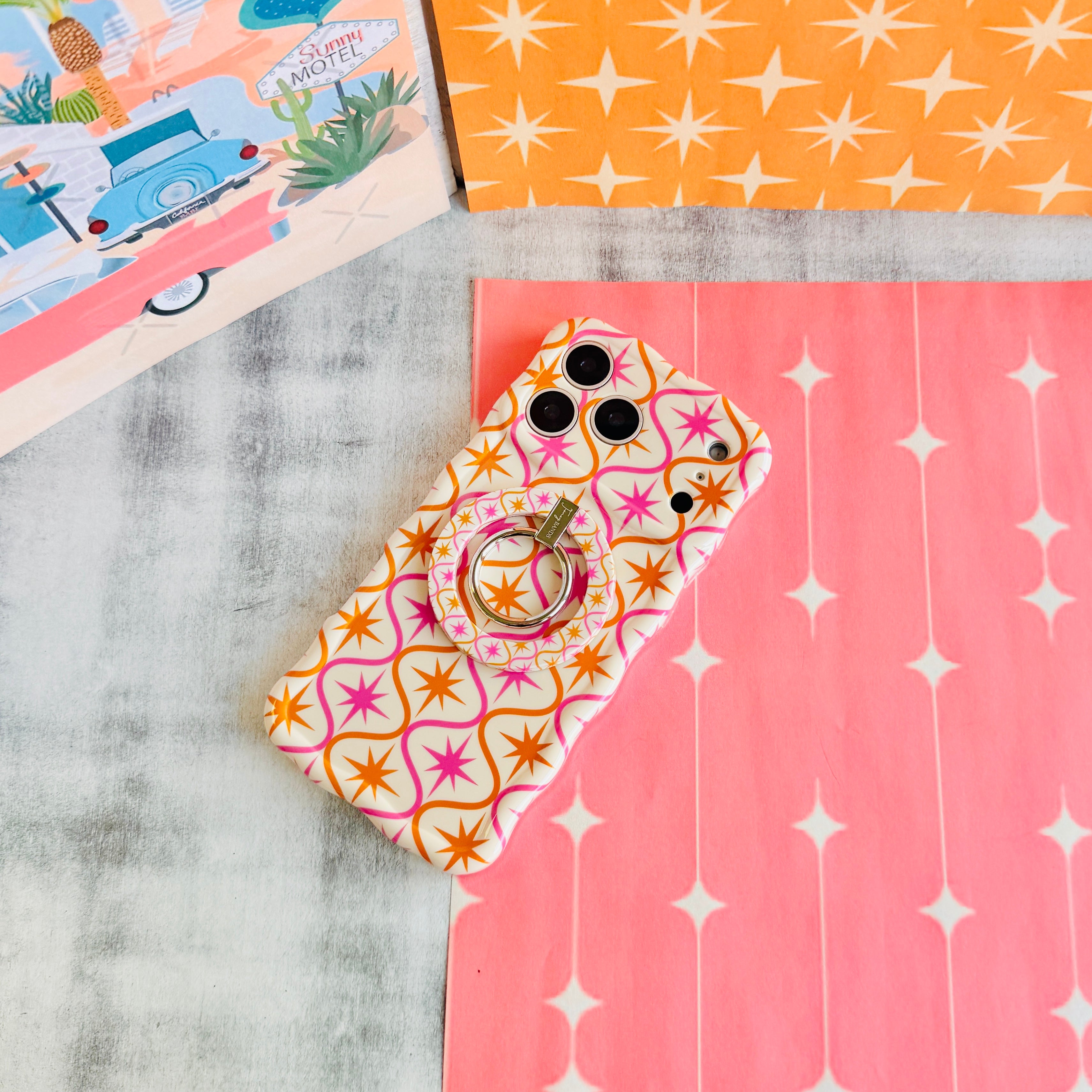 Trendy wavy iPhone case featuring a pink and orange starburst geometric pattern on a cream background with a high-gloss finish.