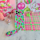 Merry & Bright, Totally! iPhone case with its Christmas tree scrunchie wrist strap on white marble, with a pink tinsel tree and confetti ornaments