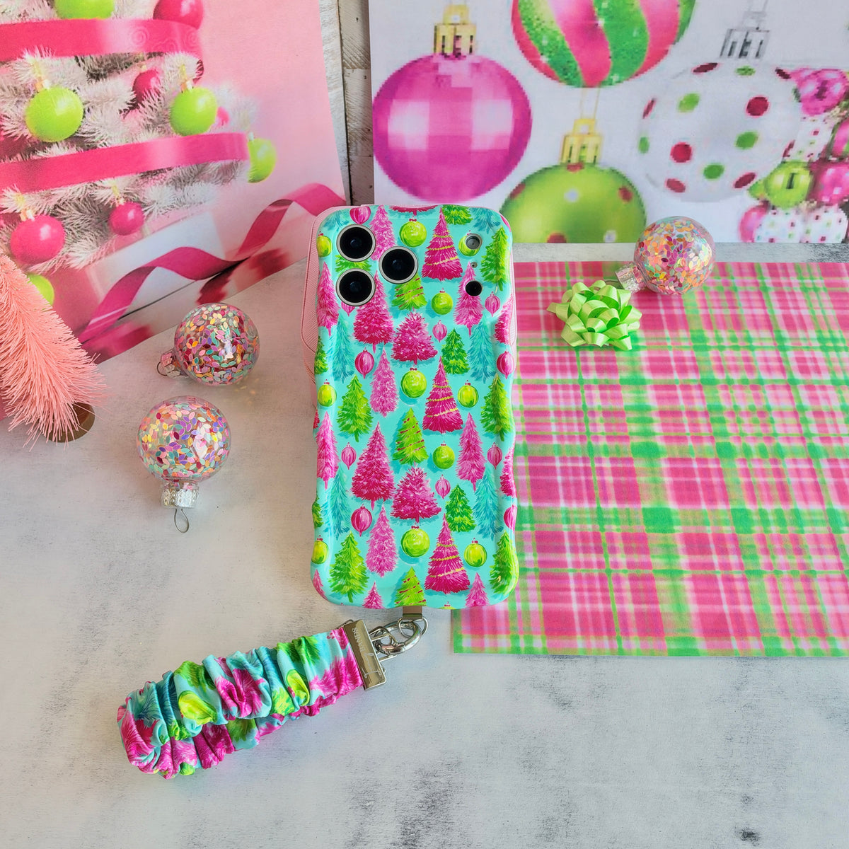 Merry & Bright, Totally! iPhone case with its Christmas tree scrunchie wrist strap on white marble, with a pink tinsel tree and confetti ornaments