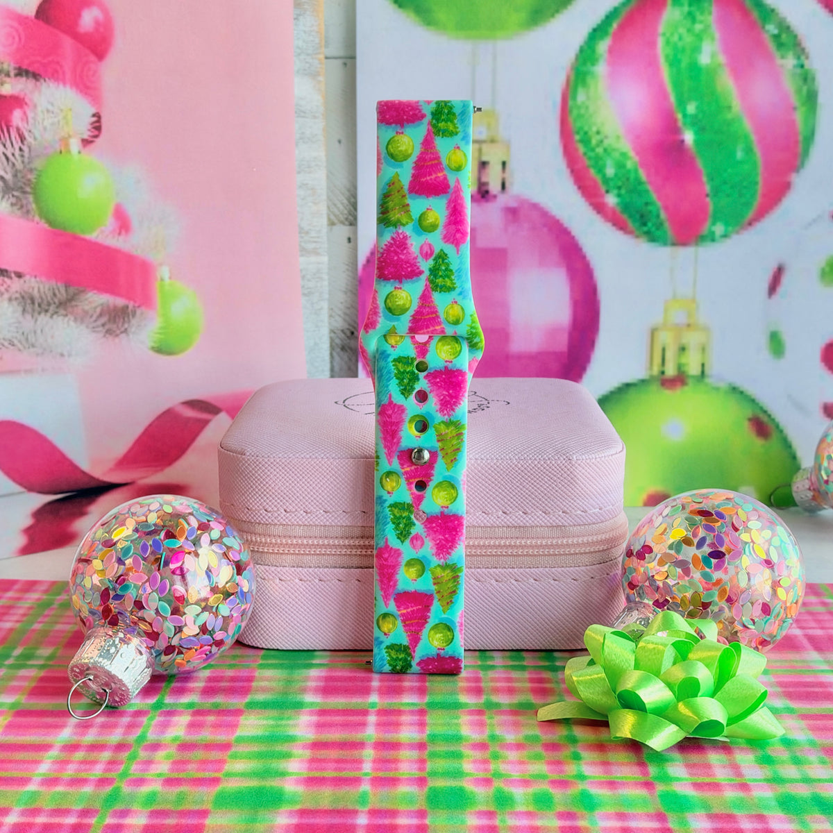 Single buckled Merry & Bright, Totally! Samsung watch band strap standing on a pink jewelry box between confetti ornaments and a lime bow