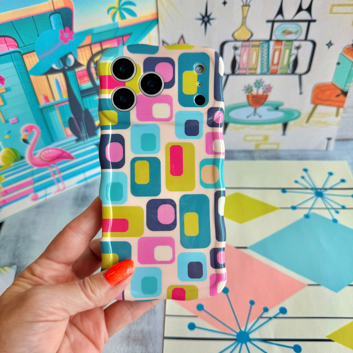 Hand holding the Mod Mood Wavy Luxe MagSafe iPhone case with teal, lime, pink and navy rounded squares on a retro atomic starburst backdrop