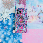 Sugarplum Square MagSafe grip ring snapped onto the matching Christmas village iPhone case, on blue snowflake paper with glitter snowflakes