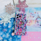 Sugarplum Square Hold It Fancy MagSafe grip ring snapped onto the matching Christmas village iPhone case, on blue snowflake paper with glitter snowflakes