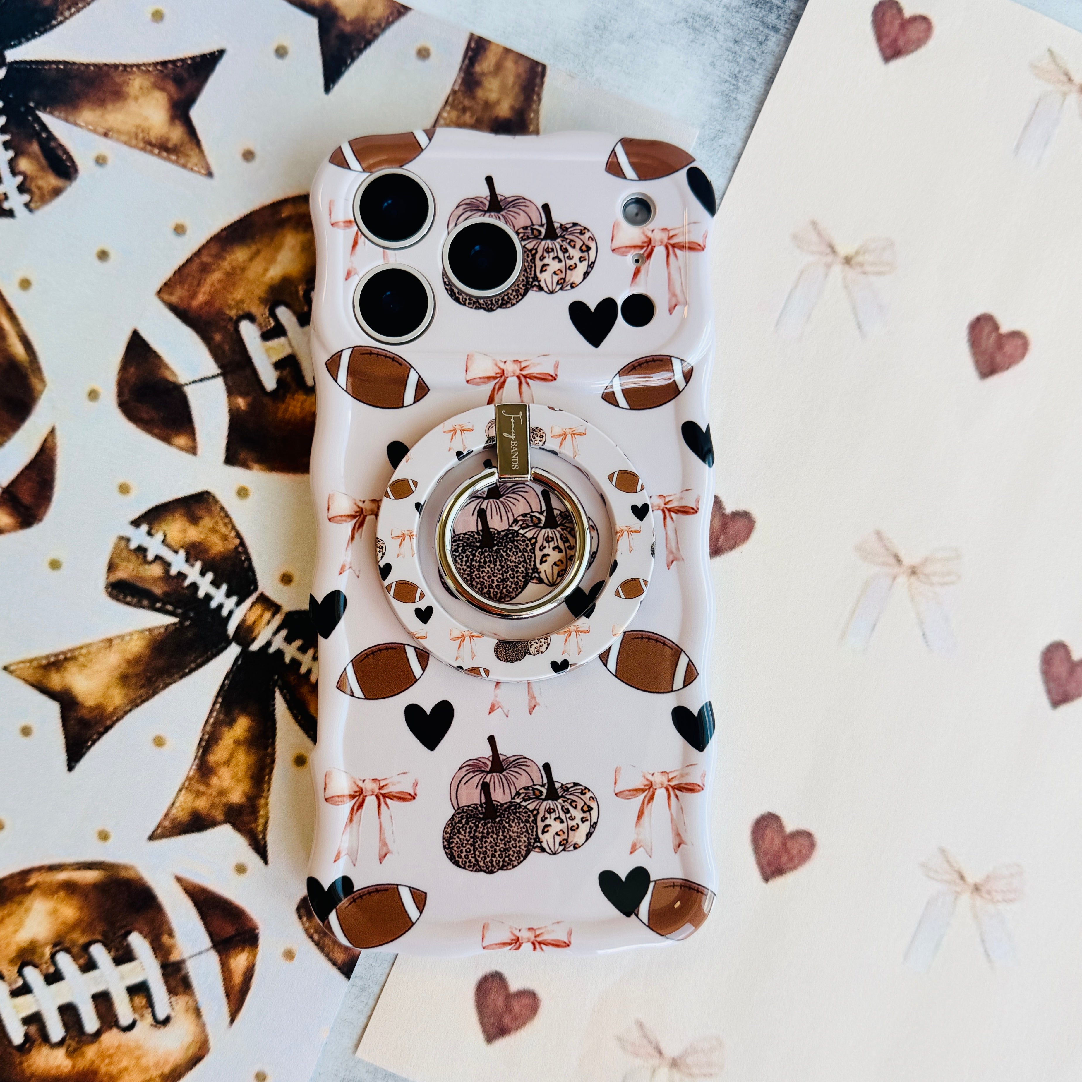Game Day Darling Hold It Fancy MagSafe grip ring with a cream coquette print of footballs, leopard pumpkins, bows and hearts from Fancy Bands