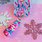 Sugarplum Square scrunchie phone wrist strap clipped below the matching iPhone case on pink paper with white and pink glitter snowflakes