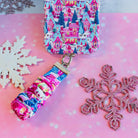 Sugarplum Square scrunchie phone wrist strap clipped below the matching Christmas village iPhone case on pink paper with glitter snowflakes