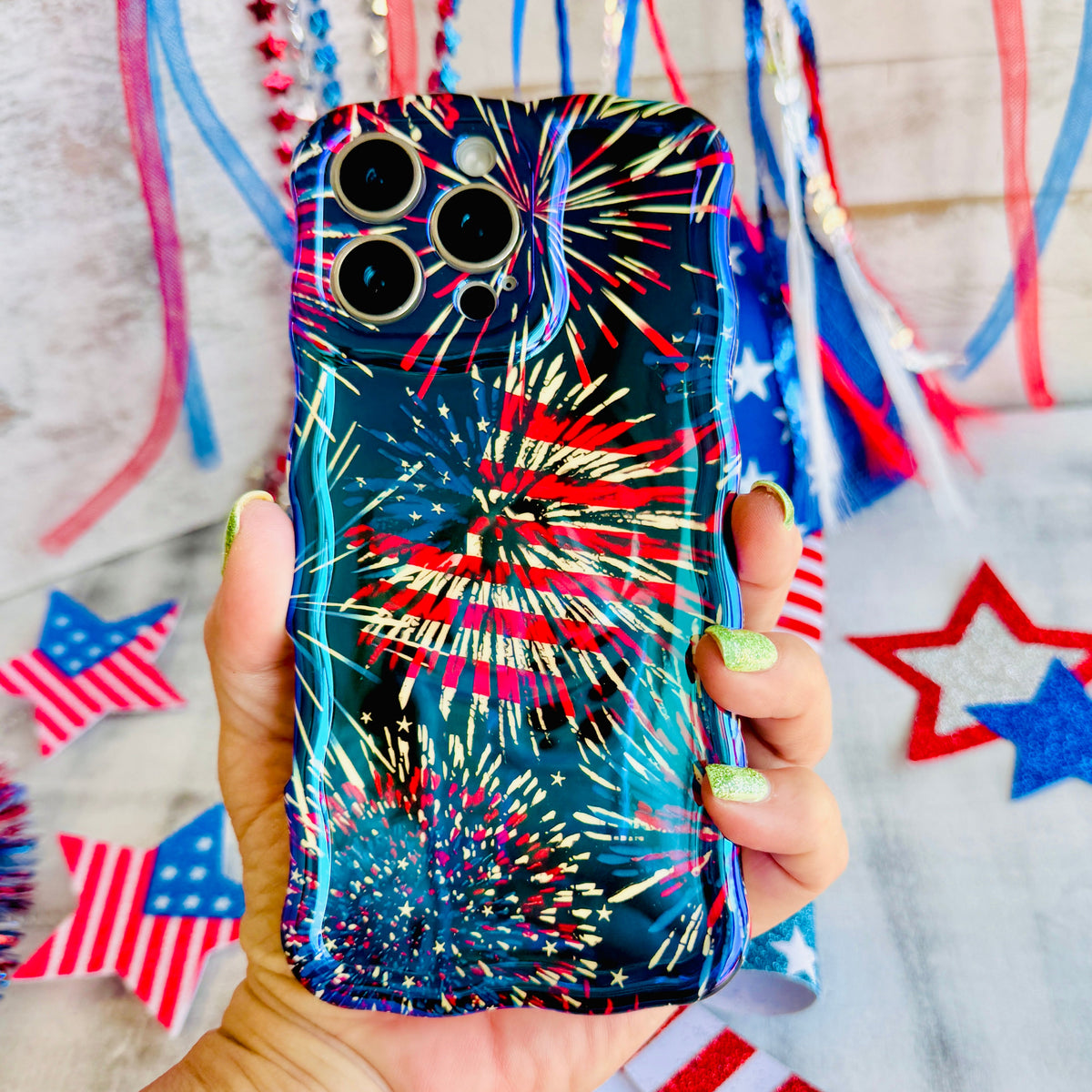 Hand holding the USA Fireworks Wavy Luxe MagSafe iPhone case, red white and blue firework bursts on a navy sky