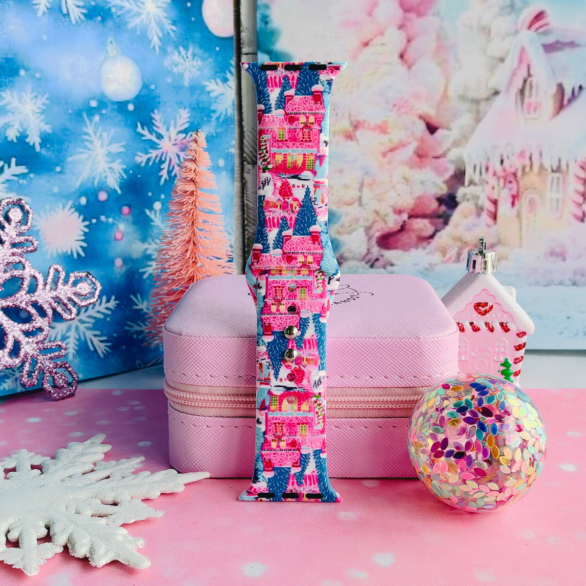 Single Sugarplum Square Apple Watch band strap standing on a pink jewelry box with a pink bottle-brush tree and snowy village backdrop