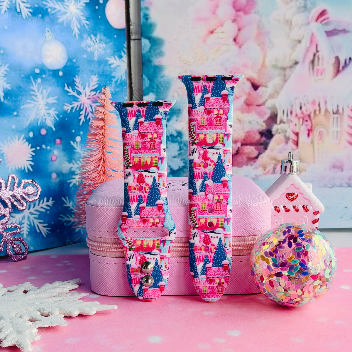 Sugarplum Square Apple Watch band buckled and standing on a pink jewelry box beside a confetti ornament and a pink gingerbread house
