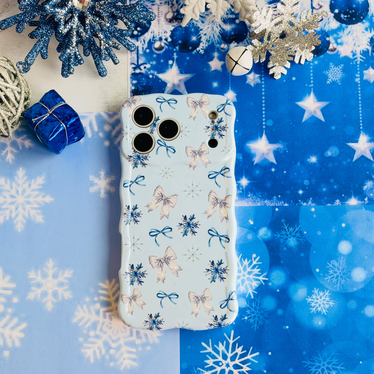 Snow Pretty In Blue iPhone case lying on blue starry snowflake paper with silver tinsel balls and glitter snowflakes