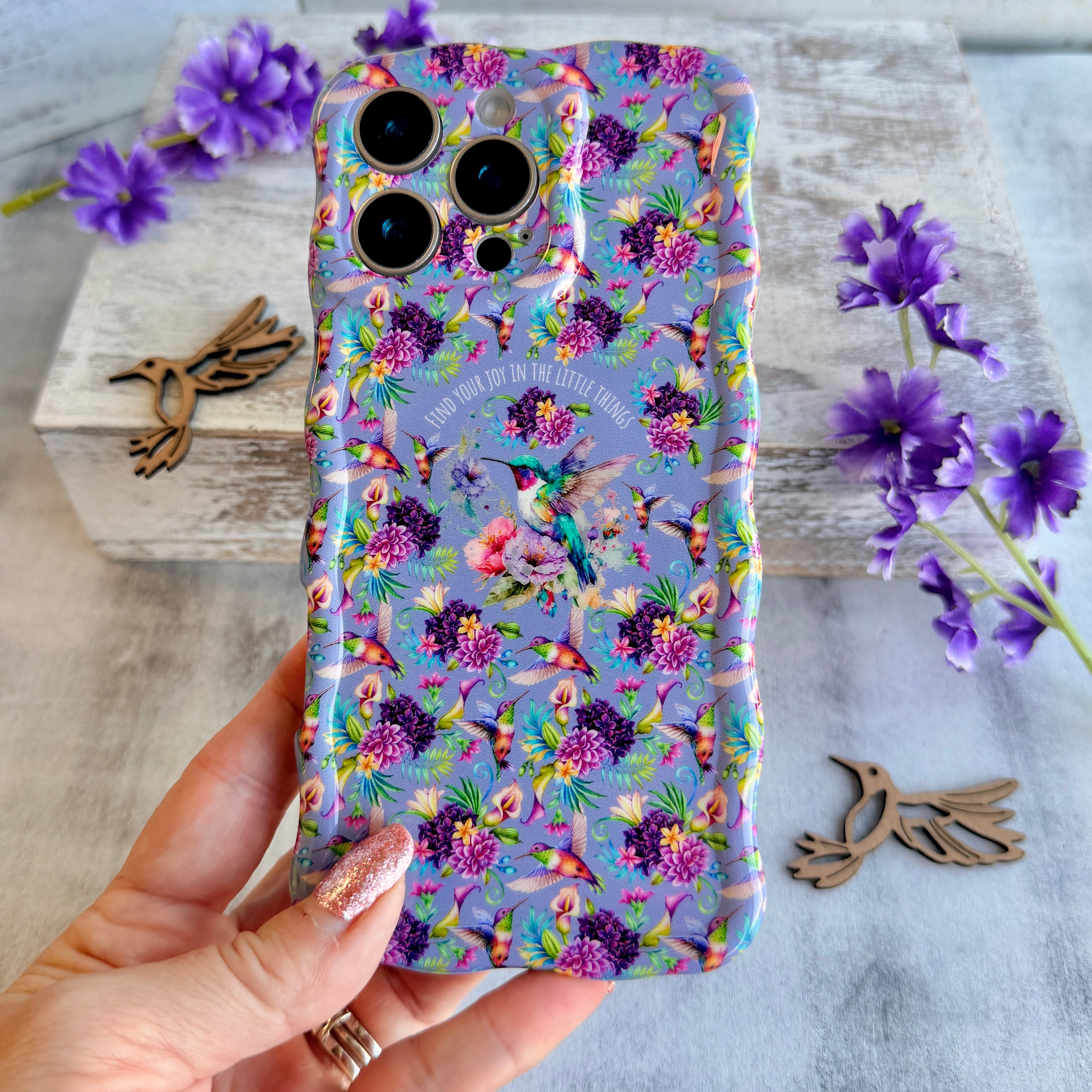 Lavender wavy iPhone case featuring colorful hummingbirds, purple flowers, and the quote Find Your Joy In The Little Things.