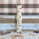 Close-up detail of Sweater Weather Sweetheart Apple Watch band showing the cream cable-knit texture, taupe bow print, and brown heart accents.