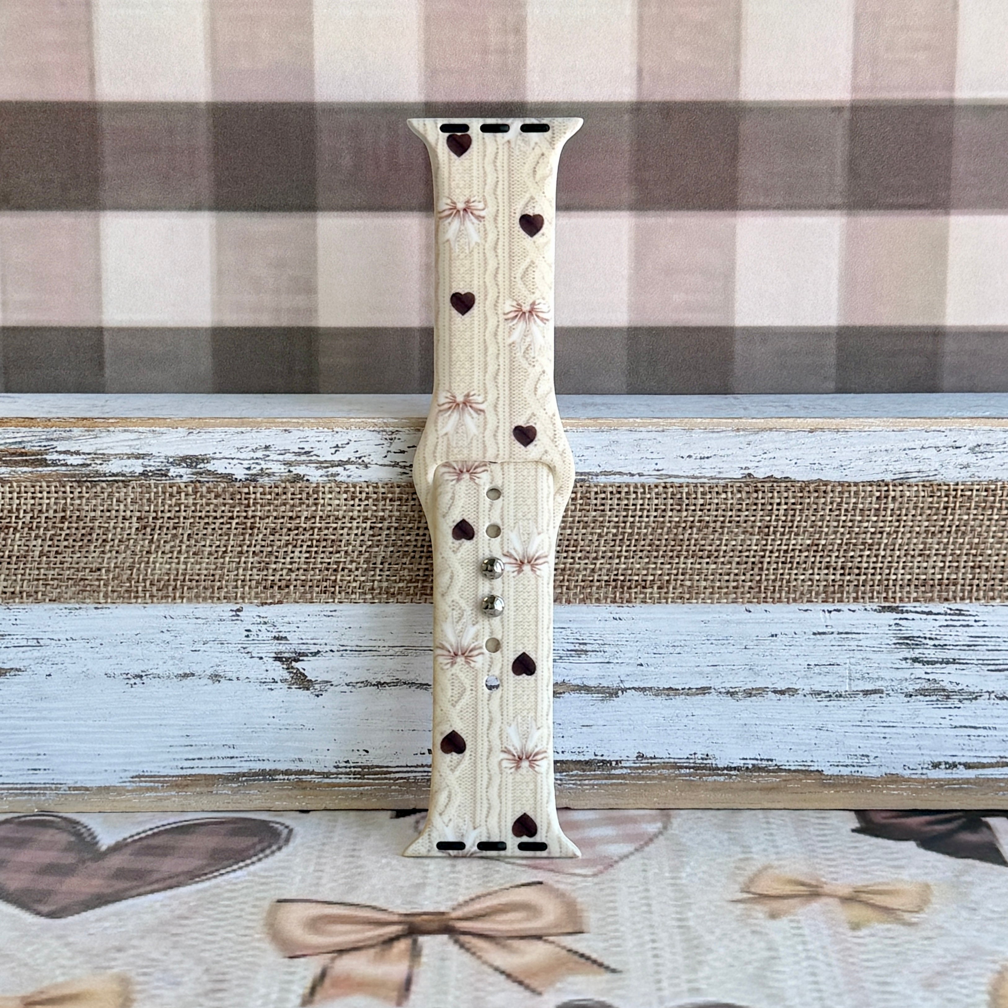Close-up detail of Sweater Weather Sweetheart Apple Watch band showing the cream cable-knit texture, taupe bow print, and brown heart accents.