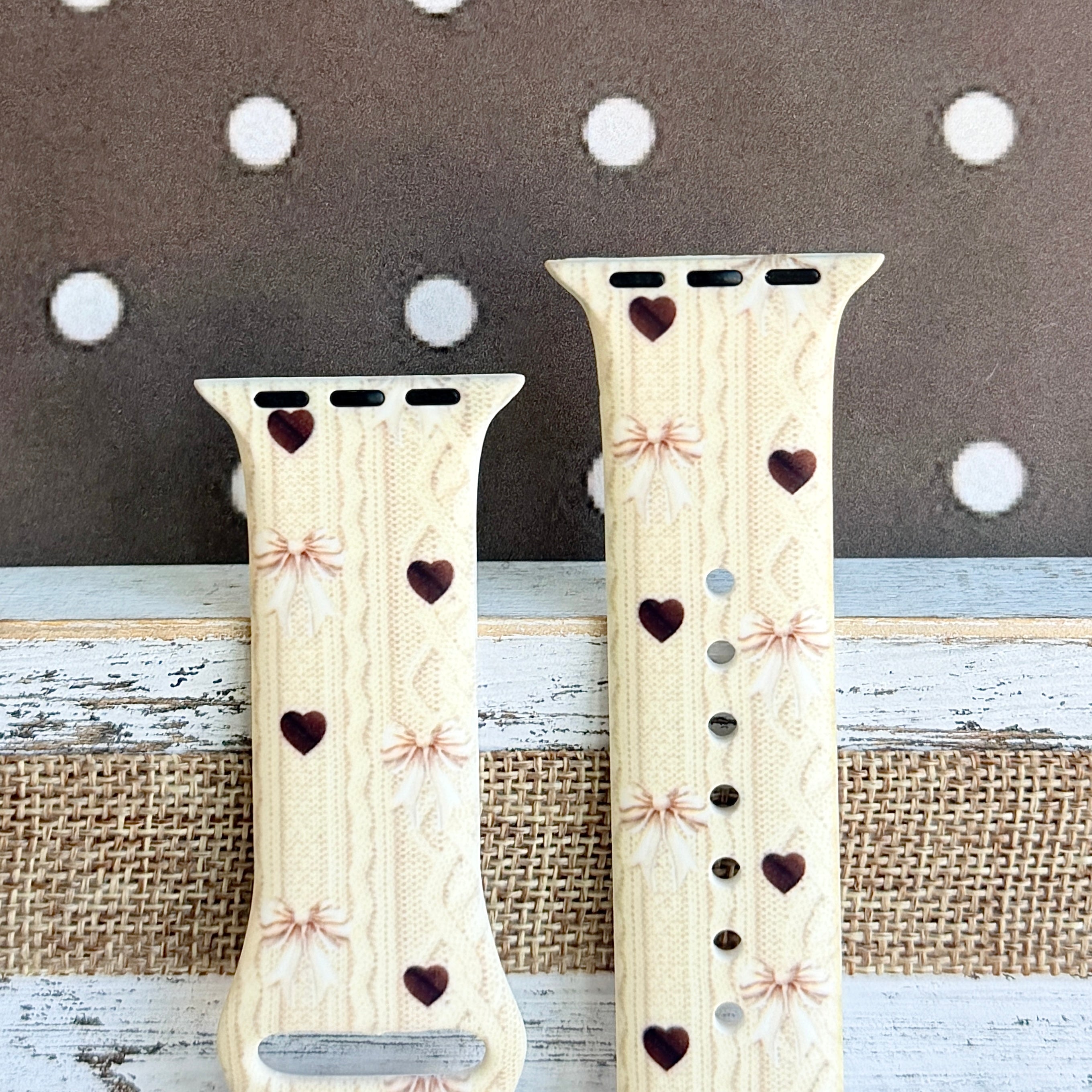 Sweater Weather Sweetheart Apple Watch band flat lay showing the cream knit print pattern with taupe bows and brown hearts across the full silicone strap.