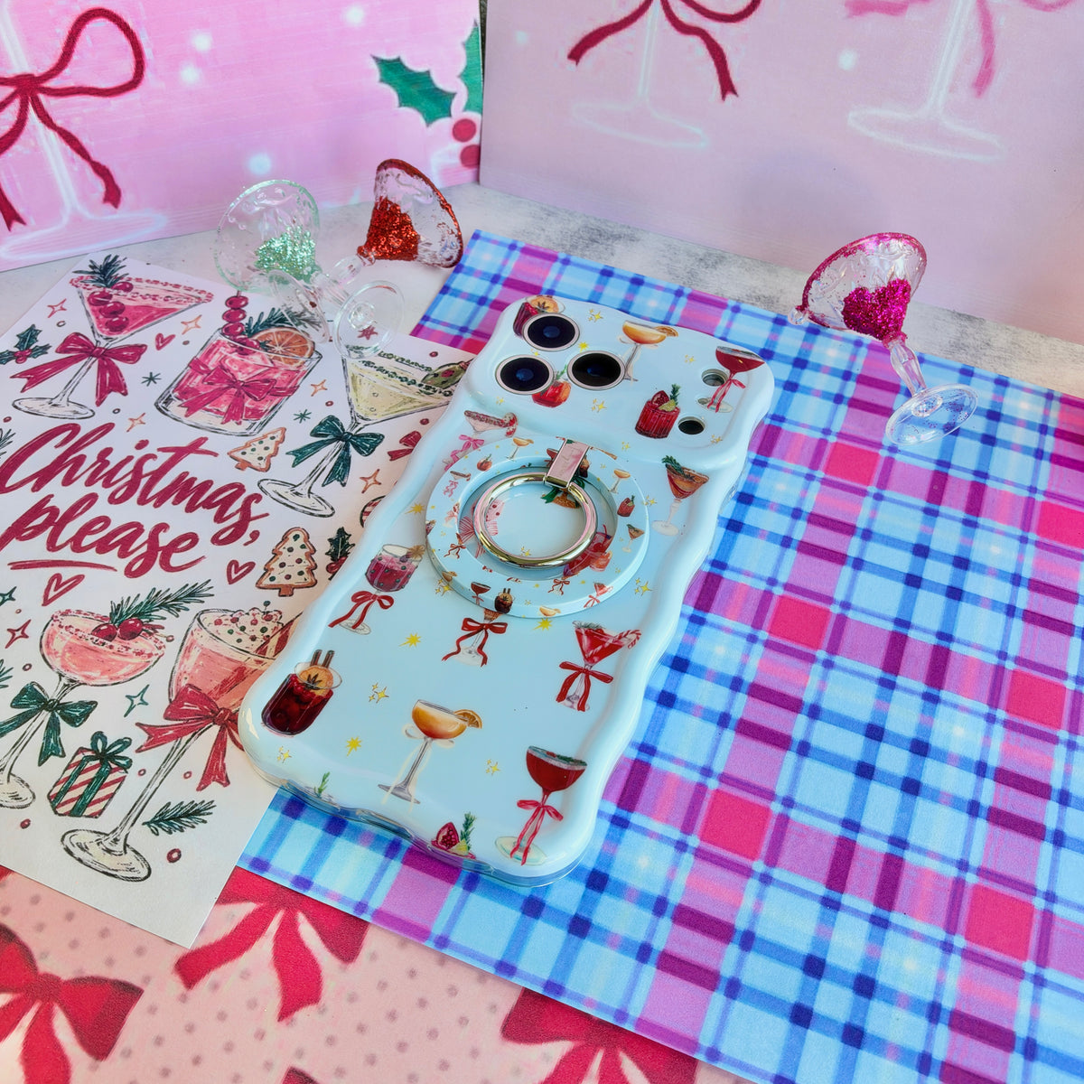 Holiday Spirits, Please? iPhone case with the matching grip ring snapped on, on pink and blue plaid with glitter-rimmed cocktail glass ornaments