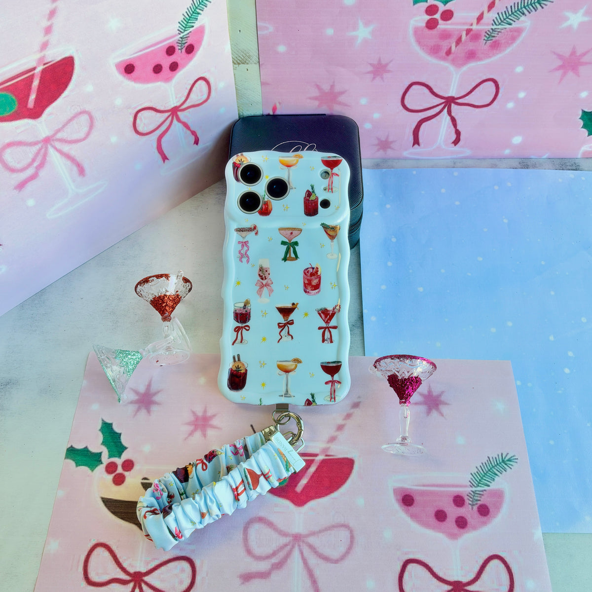 Holiday Spirits, Please? iPhone case with its cocktail print scrunchie wrist strap on pink and blue bow paper
