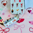 Holiday Spirits, Please? scrunchie phone wrist strap clipped below the matching cocktail print iPhone case on pink cocktail paper