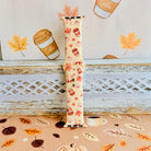 Falling in Love a Latte silicone Apple Watch band standing full length against an illustrated coffee cup and autumn leaf backdrop.