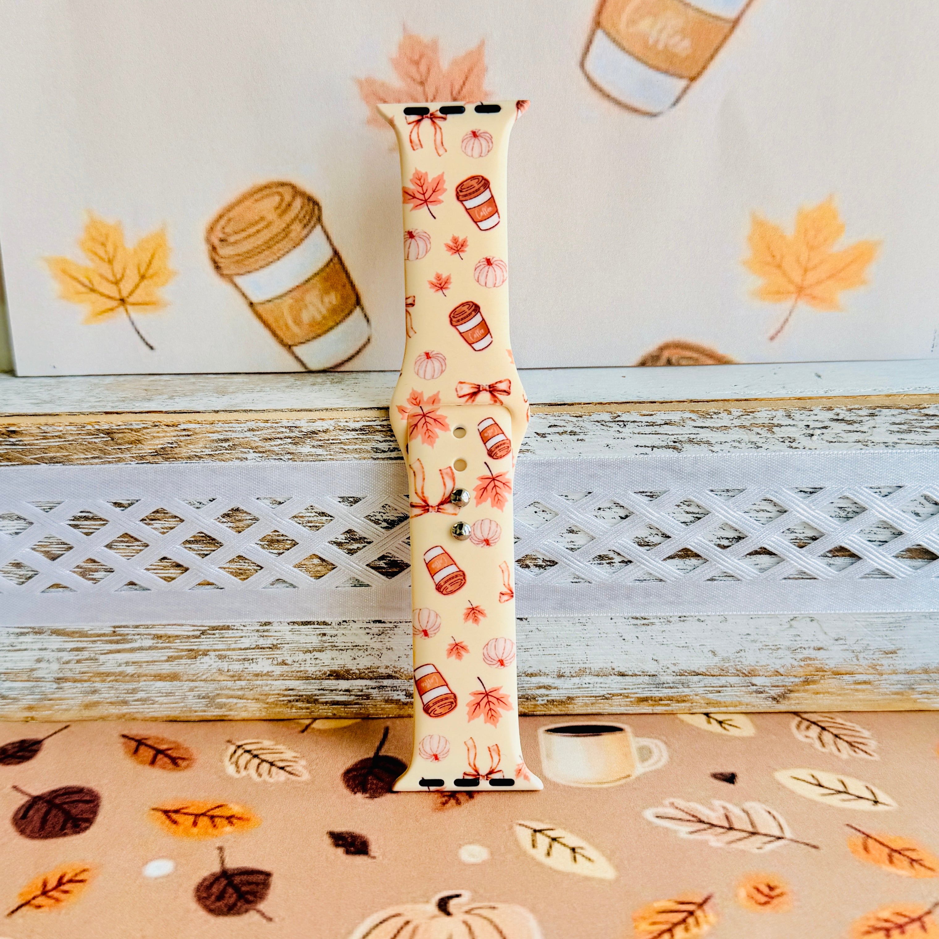 Falling in Love a Latte silicone Apple Watch band standing full length against an illustrated coffee cup and autumn leaf backdrop.