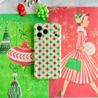 Tinsel & Stardust iPhone case lying on retro Christmas paper with a vintage shopping-girl print, a Joy ornament and a lime green gift bow
