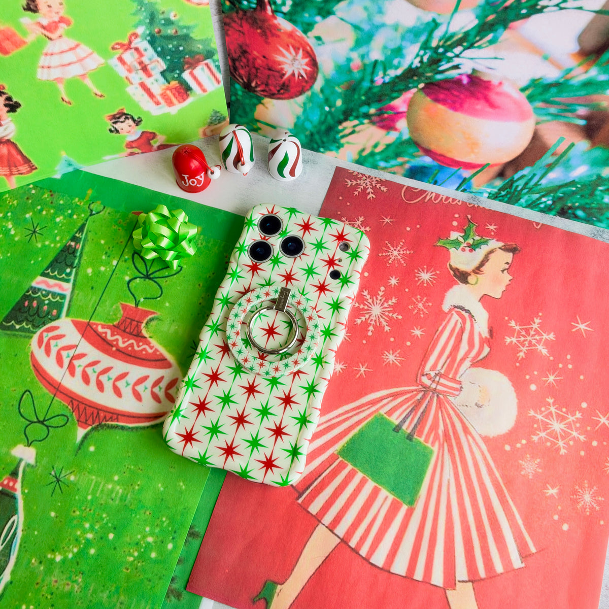 Tinsel & Stardust iPhone case with the matching starburst grip ring snapped on, on vintage red and green Christmas wrapping paper