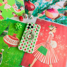 Tinsel & Stardust Hold It Fancy MagSafe grip ring snapped onto the matching retro starburst iPhone case, on vintage red and green Christmas paper