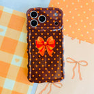 Spotted Looking Cute Wavy Luxe MagSafe iPhone case flat lay on orange gingham, showing the full polka dot print, orange bow, and sculpted wavy edge.